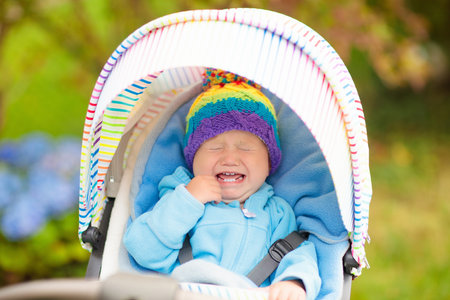 Baby in stroller on a walk in autumn park. Adorable little boy with knitted hat and jacket sitting in colorful pushchair under warm blanket. Fall outdoor fun for kids. Child in buggy on winter stroll.の写真素材