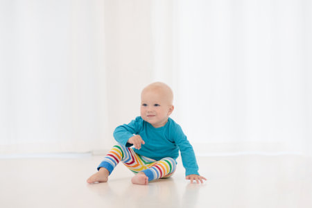 Adorable baby boy learning to crawl and playing with colorful motion toy in white sunny bedroom. Cute laughing child crawling on a play mat. Nursery, clothing and toys for little kids.の写真素材