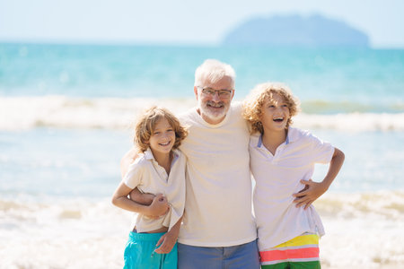 Grandfather and kids play on summer beach. Family day outdoor. Grandparent and grandchildren travel to sea side. Generation love. Active senior man playing with grandson. Happy fit retirement.の写真素材