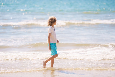 Kids playing on tropical beach. Children swim and play at sea on summer family vacation. Sand and water fun, sun protection for young children. Little boy running and jumping at ocean shore.の写真素材