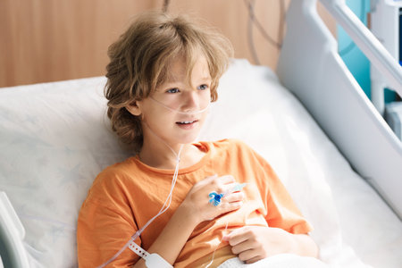 Sick child in hospital room. Kid in clinic ward. Little boy with oxygen tube and IV line in hospital bed. Pediatrician doctor examining patient. Family health care and insurance. Medicine for children.の写真素材