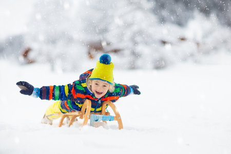 Little boy enjoying a sleigh ride. Child sledding. Toddler kid riding a sledge. Children play outdoors in snow. Kids sled in the Alps mountains in winter. Outdoor fun for family Christmas vacation.の写真素材