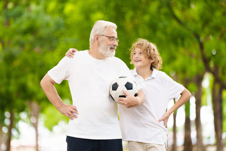 Grandfather and kids play football in sunny park. Happy family playing ball. Grandpa and children play soccer. Generation love. Active senior man with little boy. Grandchildren visit grandparents.の写真素材