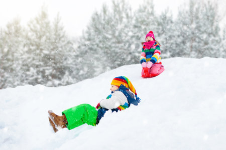 Little girl enjoying a sleigh ride. Child sledding. Toddler kid riding a sledge. Children play outdoors in snow. Kids sled in the Alps mountains in winter. Outdoor fun for family Christmas vacation.の写真素材