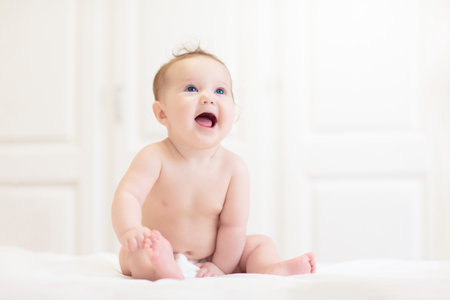 Baby in diaper in white sunny bedroom. Newborn child relaxing in bed. Nursery for young children. Textile and bedding for kids. Family morning at home. New born kid in nappy.の写真素材