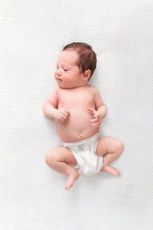 Baby in diaper in white sunny bedroom. Newborn child relaxing in bed. Nursery for young children. Textile and bedding for kids. Family morning at home. New born kid in nappy.の写真素材