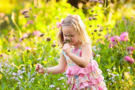 Little girl playing with flowers in the garden. Kids play outdoors in summer. Children gardening. Child planting flower in the backyard. Gardener at work. Kid working with plants.の写真素材