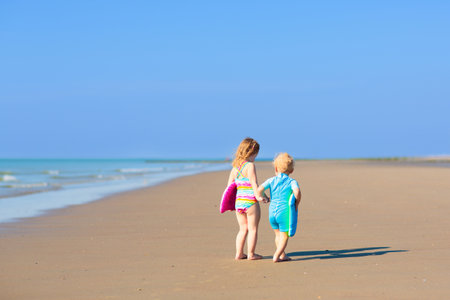 Kids playing on tropical beach. Water splash fun. Little boy splashing in sea waves. Children swim and play on summer family vacation. Sand and water toy, sun protection for young child.の写真素材