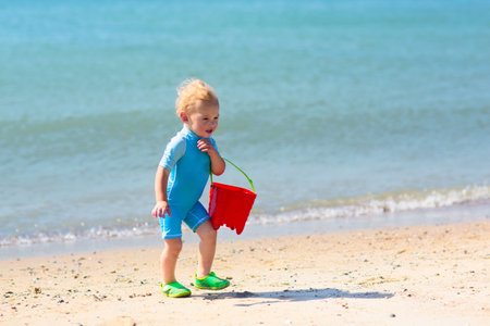 Kids playing on tropical beach. Water splash fun. Little boy splashing in sea waves. Children swim and play on summer family vacation. Sand and water toy, sun protection for young child.の写真素材