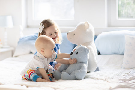 Little girl and baby boy, brother and sister playing in parents bed. Family with children in the morning. Kids play in white bedroom. Nursery crib bedding and textile for young child. Siblings love.の写真素材