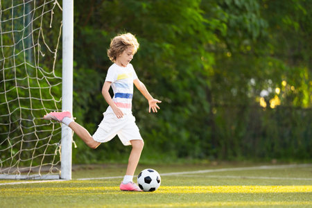 Child playing football. Kids play soccer on outdoor pitch. Little boy kicking ball in summer park. Healthy activity for young children. School sport club team. Football junior league.の写真素材