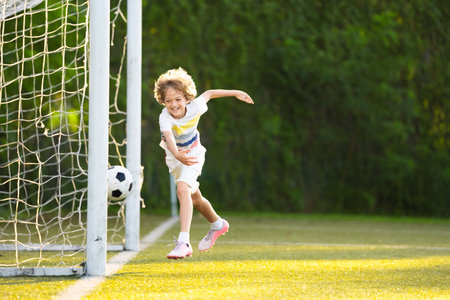 Child playing football. Kids play soccer on outdoor pitch. Little boy kicking ball in summer park. Healthy activity for young children. School sport club team. Football junior league.の写真素材