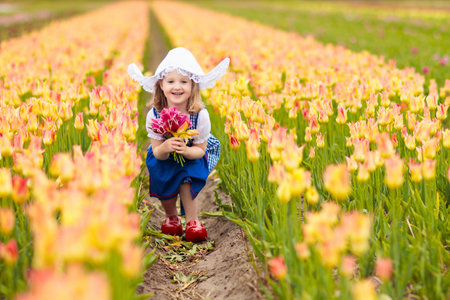 Happy Dutch children playing in blooming tulip flowers field. Boy and girl wearing traditional national costume, wooden clogs and hat play with tulips next to a windmill in Holland, Netherlandsの写真素材