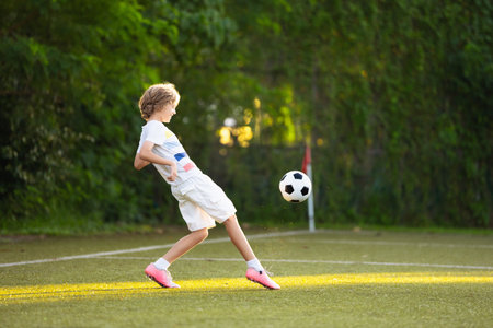 Child playing football. Kids play soccer on outdoor pitch. Little boy kicking ball in summer park. Healthy activity for young children. School sport club team. Football junior league.の写真素材