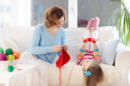 Mother and daughter knitting woolen scarf. Mom teaching child to knit. Crafts and hobbies for parents and children. Toddler girl kid with wool yarn in a basket. Knitted clothing for family with children.の写真素材