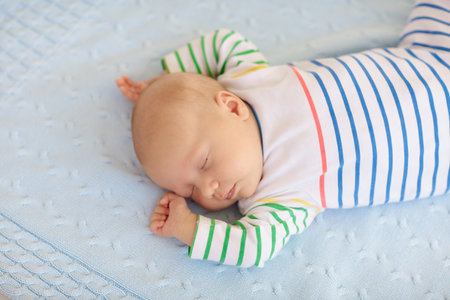 Adorable baby in white sunny bedroom. Newborn child relaxing in bed. Nursery for young children. Textile and bedding for kids. Family morning at home. New born kid during tummy time with toy bear.の写真素材