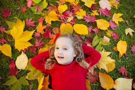 Happy children playing in beautiful autumn park on warm sunny fall day. Kids play with golden maple leaves.の写真素材