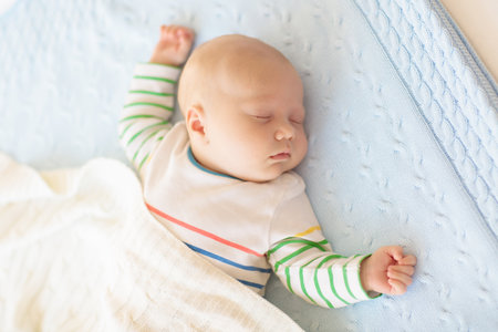 Adorable baby in white sunny bedroom. Newborn child relaxing in bed. Nursery for young children. Textile and bedding for kids. Family morning at home. New born kid during tummy time with toy bear.の写真素材