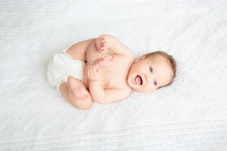 Baby in diaper in white sunny bedroom. Newborn child relaxing in bed. Nursery for young children. Textile and bedding for kids. Family morning at home. New born kid in nappy.の写真素材