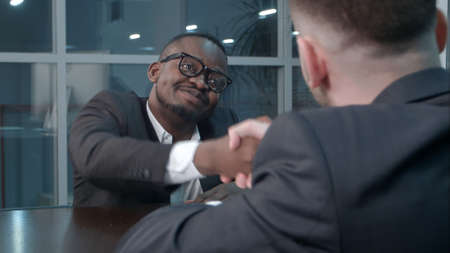 Interracial businessmen shaking hands in business hall, smilingの写真素材