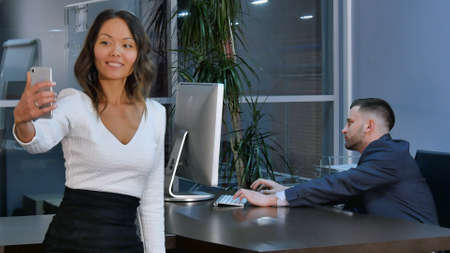 Beautiful asian woman taking selfie on smartphone, working in office. Professional shot in 4K resolution. 085. You can use it e.g. in your commercial video, business, presentation, broadcast video.の写真素材