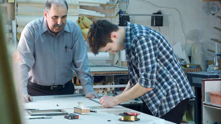 Young trainee constructing a frame behind the desk in frame workshop. Professional shot in 4K resolution. 083. You can use it e.g. in your commercial video, business, presentation, broadcast video.の写真素材