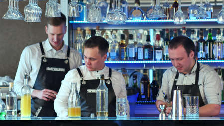 Three bartenders serving cocktails and working in a classy barの写真素材