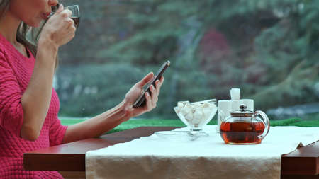Woman using mobile phone and drinking tea in cafeの写真素材