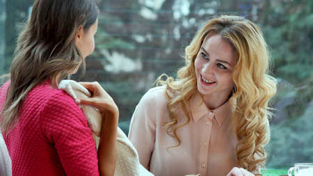 Beautiful young woman showing her brand new clothes to her friend while both sitting in cafeの写真素材