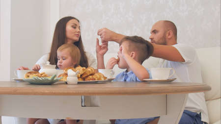 Happy young family enjoying tea with sweets at restaurant or cafe or homeの写真素材