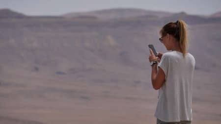 Young woman taking panoramic photo of the desert crater on her phoneの写真素材
