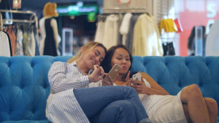 Happy young women with smartphones and shopping bags talking in mall