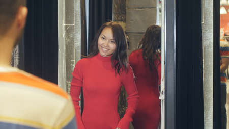 Beautiful young brunette showing red dress to her boyfriend in dressing roomの写真素材