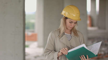 Young female architect construction engineer at a construction site eximaining documentsの写真素材