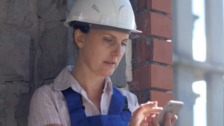 A young construction female worker sits at a site and works on a smartphoneの写真素材