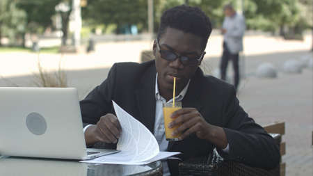Business man works in outdoor coffee shop with his laptop and wireless internet connection, drinking juiceの写真素材