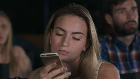 Shot of a beautiful young female texting during movies at the local cinemaの写真素材