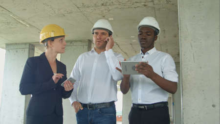 Executive team on construction site reviewing with tablet, smartphone, formal dressed people reading construction tabletの写真素材