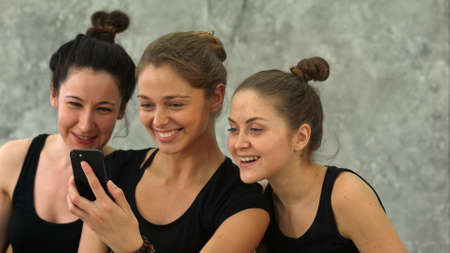 Three young women browsing Internet using smartphone after workout at yoga classの写真素材