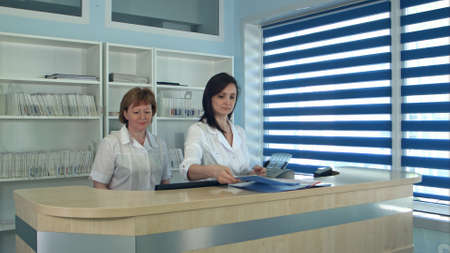 Smiling female doctors standing at the reception desk in hospitalの写真素材