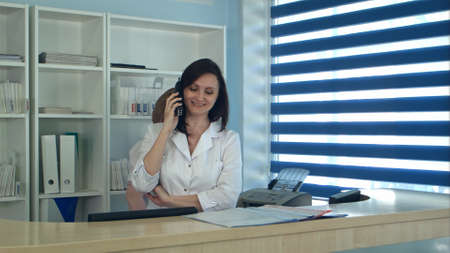 Smiling female nurse answering phone call at the reception deskの写真素材