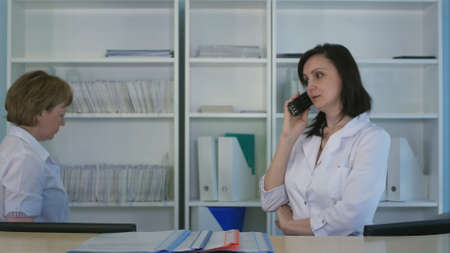 Smiling female nurse answering phone at the hospital reception deskの写真素材