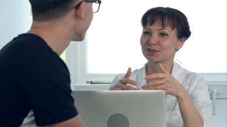 Friendly female doctor consulting male patient sitting at desk with laptopの写真素材