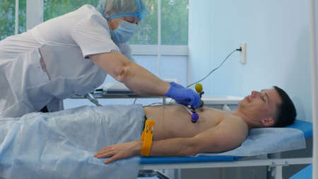 Nurse in gloves and mask removing ECG pads off the male patientの写真素材