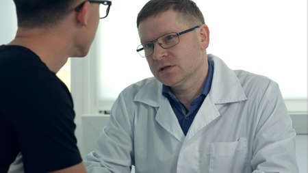 Male doctor in glasses consulting male patientの写真素材