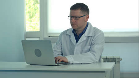 Male doctor working on laptop computer on white desk in hospitalの写真素材