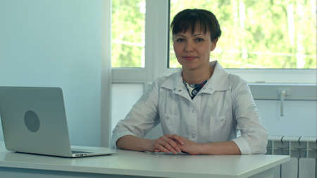 Female doctor working at office desk with laptop and smiling at cameraの写真素材