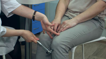 Neurologist testing reflexes on female patient using hammerの写真素材