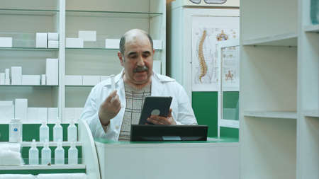 Senior pharmacist having video chat with client using tablet pc in drug storeの写真素材