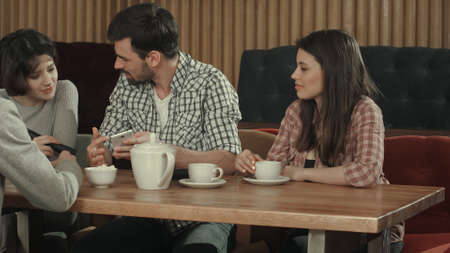 Group of young people sitting at a cafe, talking and drinking teaの写真素材
